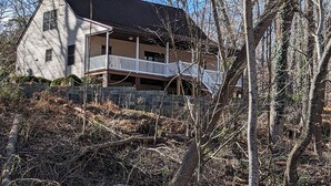 Een huis met twee verdiepingen en een balkon, omgeven door bomen en een stenen muur.