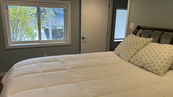 A bedroom with a large bed, a window with a view of trees, and a door leading to another room.