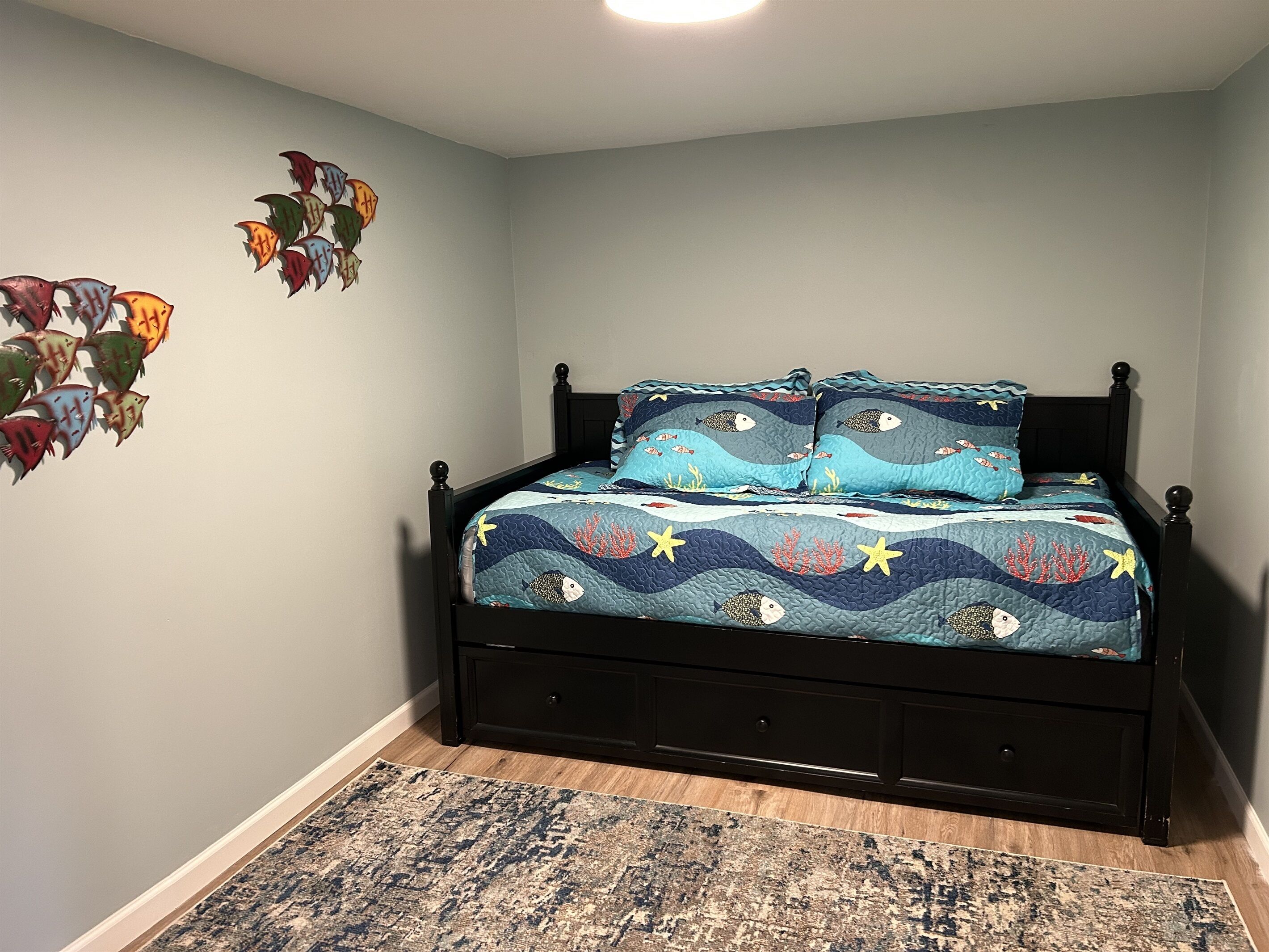 Un dormitorio con cama, mesita de noche, estante en la pared y alfombra estampada.