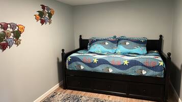 Un dormitorio con cama, mesita de noche, estante en la pared y alfombra estampada.