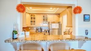 A kitchen with granite countertops, white cabinets, and a built-in refrigerator. There are wicker chairs in front of the counter and a bottle of wine on the counter. - Gulf views w/scenic elevated sundeck, heated shared pool, boat dock availability (Marathon)