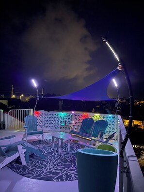 A rooftop terrace with outdoor seating, including chairs and tables, under a canopy.