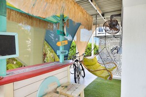 Een terras in strandstijl met een fiets, een hangstoel en een ventilator.