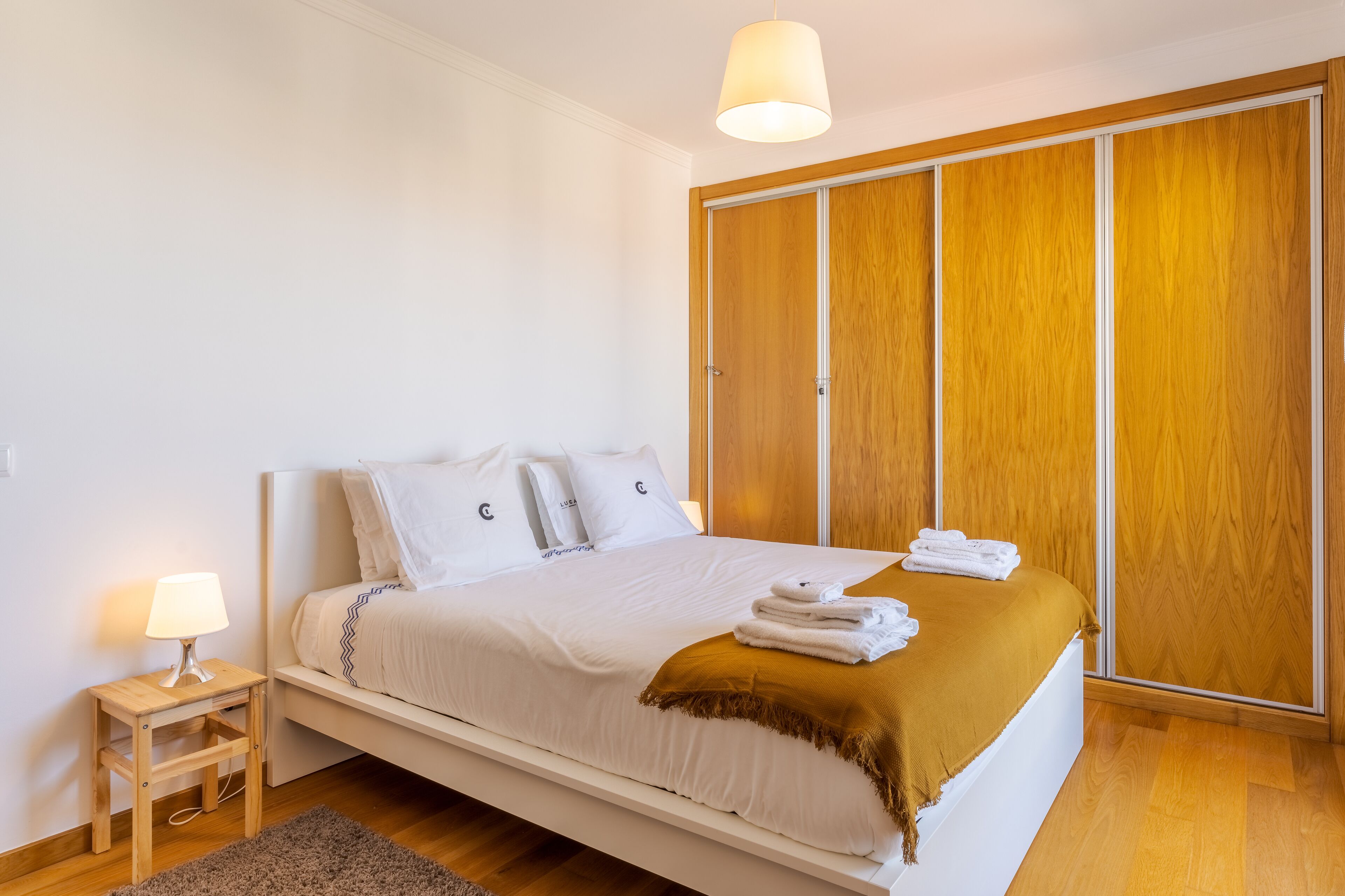 Quarto com uma cama, mesa de cabeceira, luminária, guarda-roupa e janela.