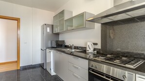 A modern kitchen with stainless steel appliances, a microwave, a kettle, and a gas stove. - Jardins do Oceano (Santa Cruz)