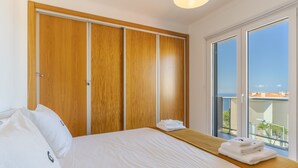 A bedroom with a large bed, wooden wardrobe, and a balcony with a view. - Jardins do Oceano (Santa Cruz)