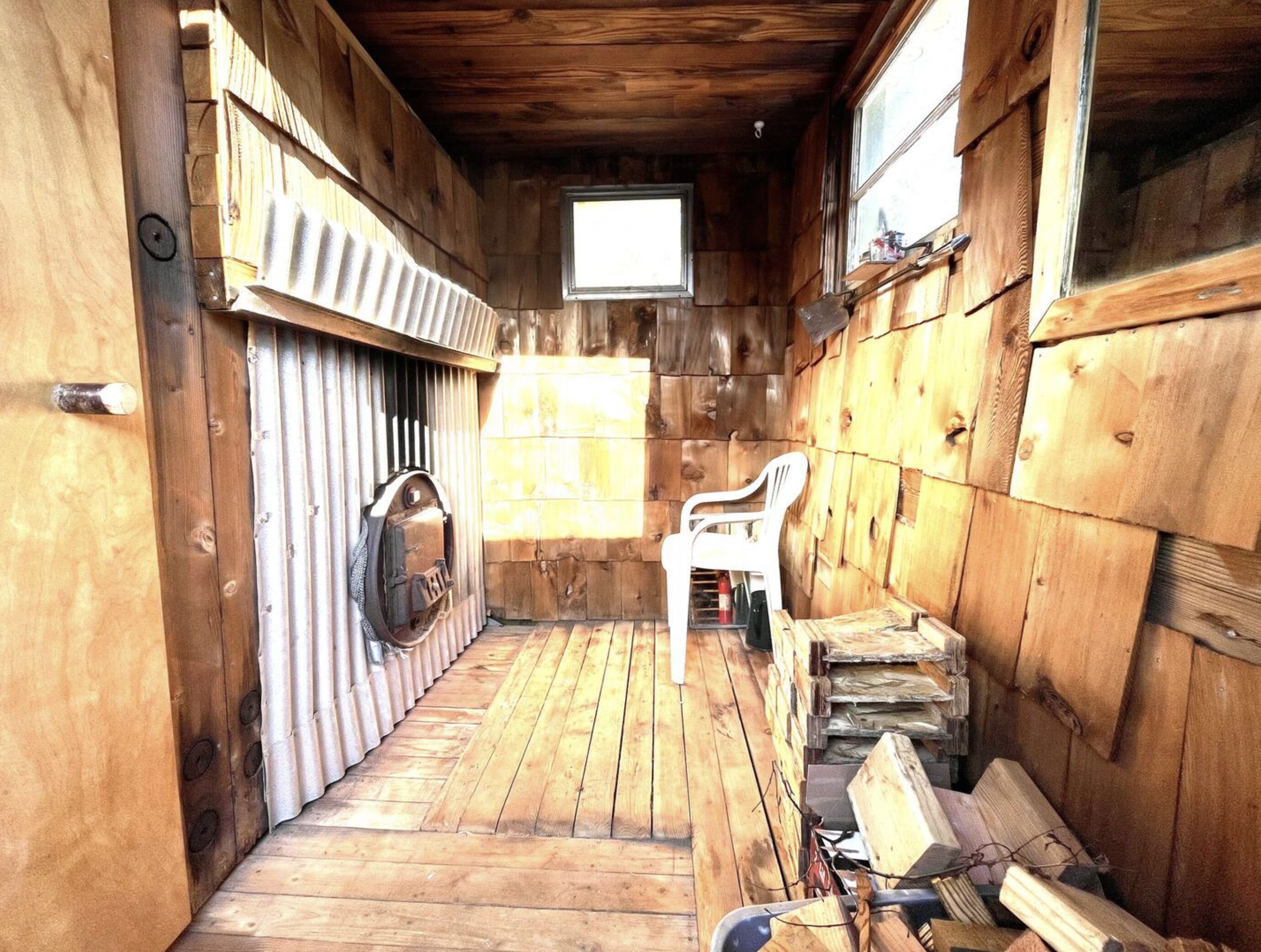 A wooden cabin interior with a small window, a wooden door, and a chair.