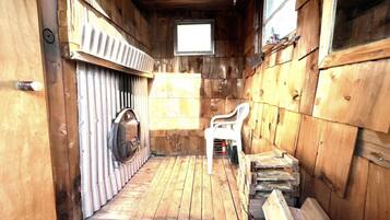 A wooden cabin interior with a small window, a wooden door, and a chair.
