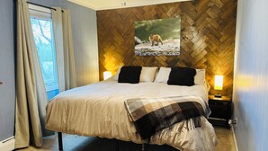 Un dormitorio con cama, ventilador de techo, mesita de noche con lámpara, ventana con cortinas y pared con diseño de espiga.