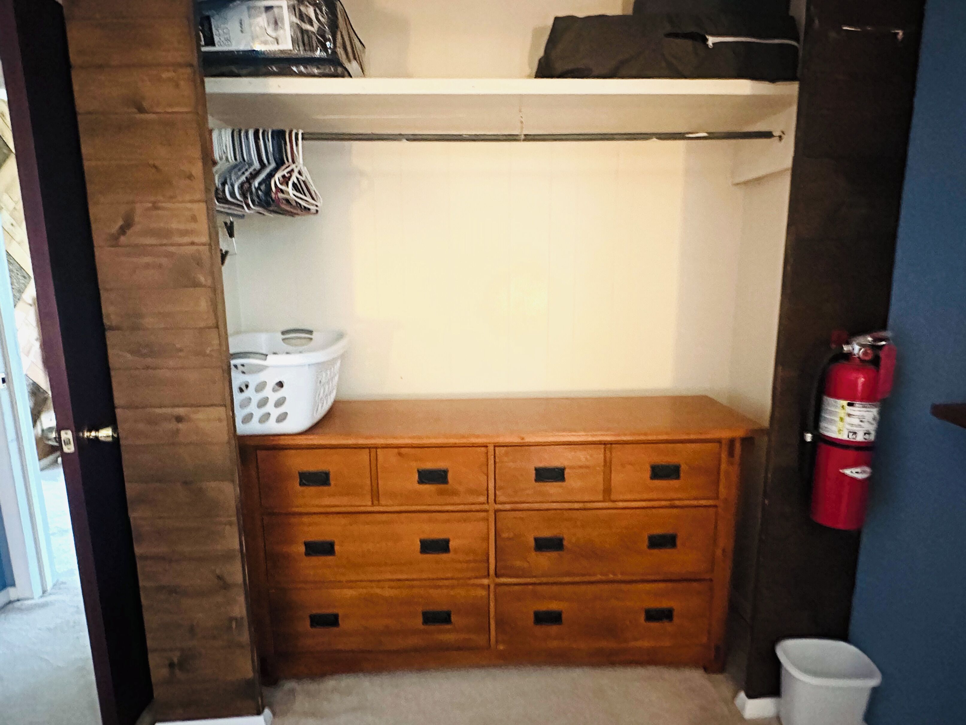 Un petit placard de rangement contenant une commode en bois, une étagère au-dessus et un extincteur sur le côté droit.