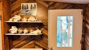 Un interior de madera con una puerta, estantes mostrando cráneos de animales y un letrero que dice '¿QUIÉN CORTÓ UNO?'.