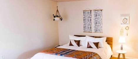 Un dormitorio con cama, lámpara colgante, panel decorativo en la pared y mesita de noche con lámpara.