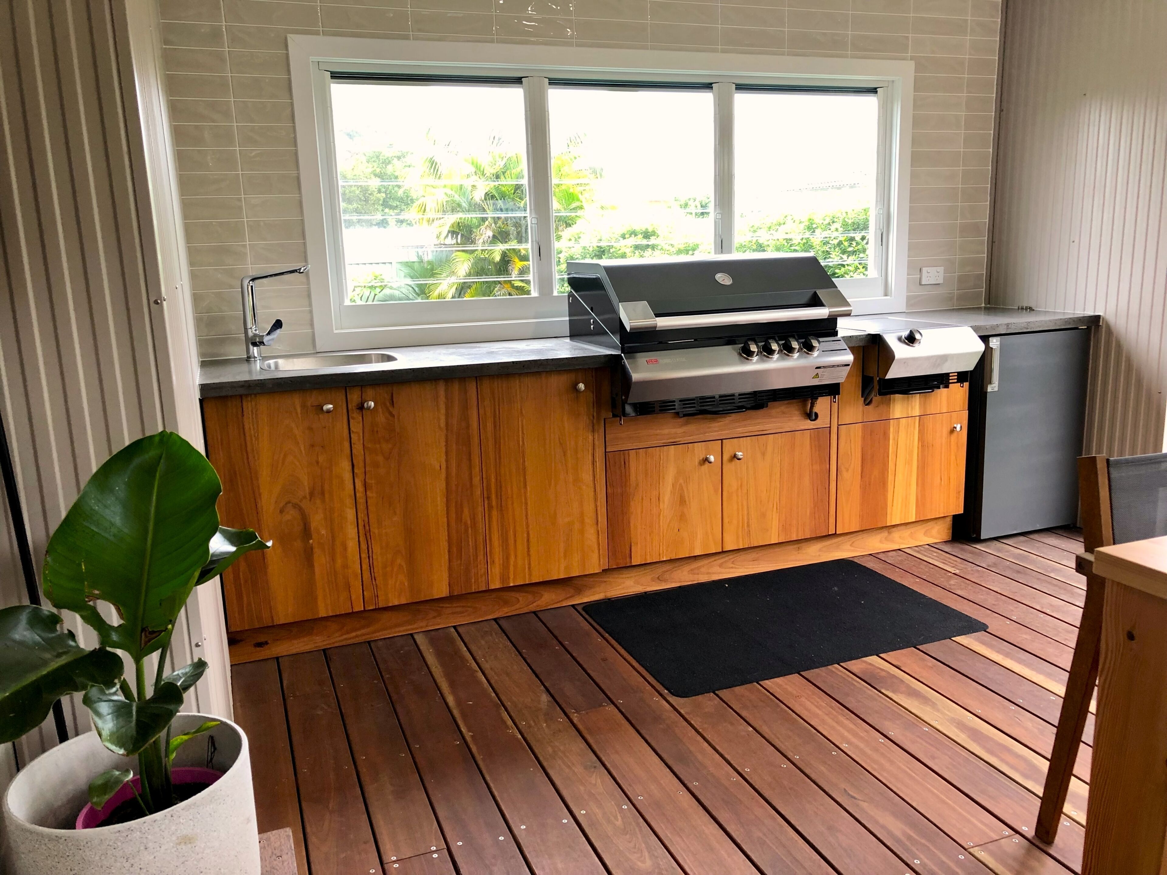 Cocina compacta con estufa a gas integrada, armarios de madera y ventana con vistas a zonas verdes.