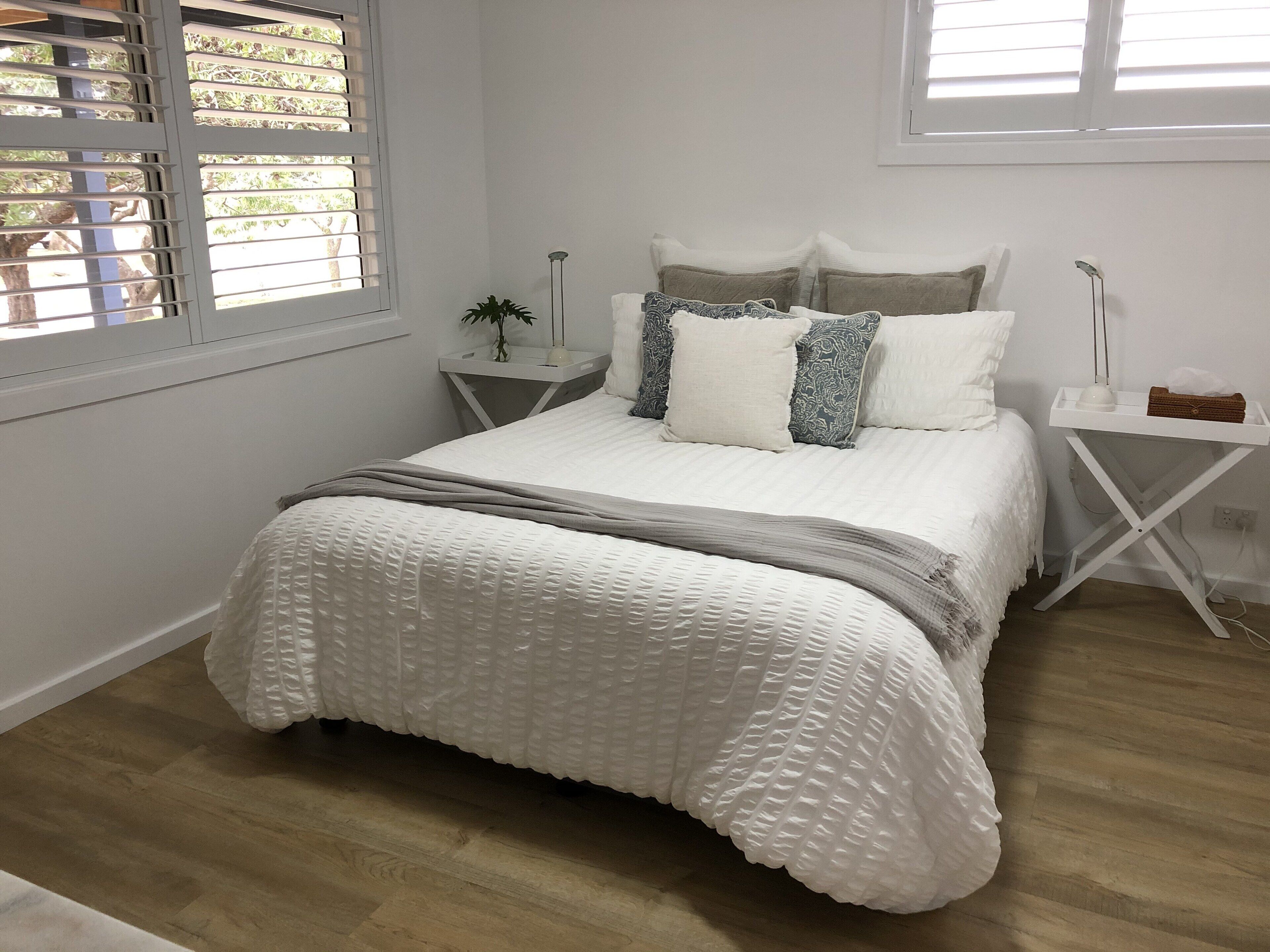 Une chambre à coucher comprenant un lit, des tables de chevet, une commode, une lampe et une fenêtre avec des stores.