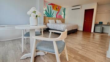 A modern hotel room with a bed, a white chair, a small table, a bathtub, and a colorful wall mural.