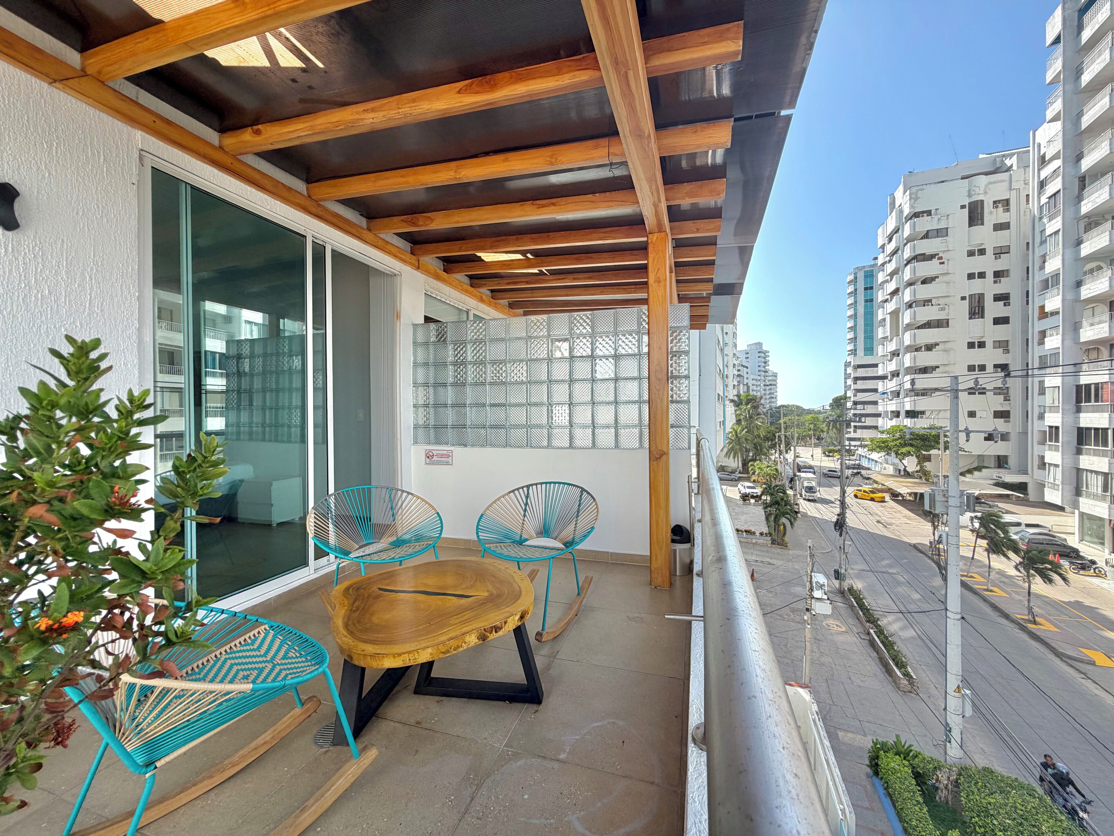 Ein Balkon mit Holzbalken, einer Glastür und Blick auf eine Straße mit Gebäuden und Autos.