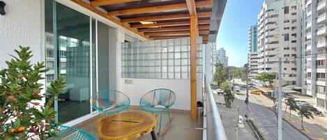 A balcony with wooden beams, a glass door, and a view of a street with buildings and cars.