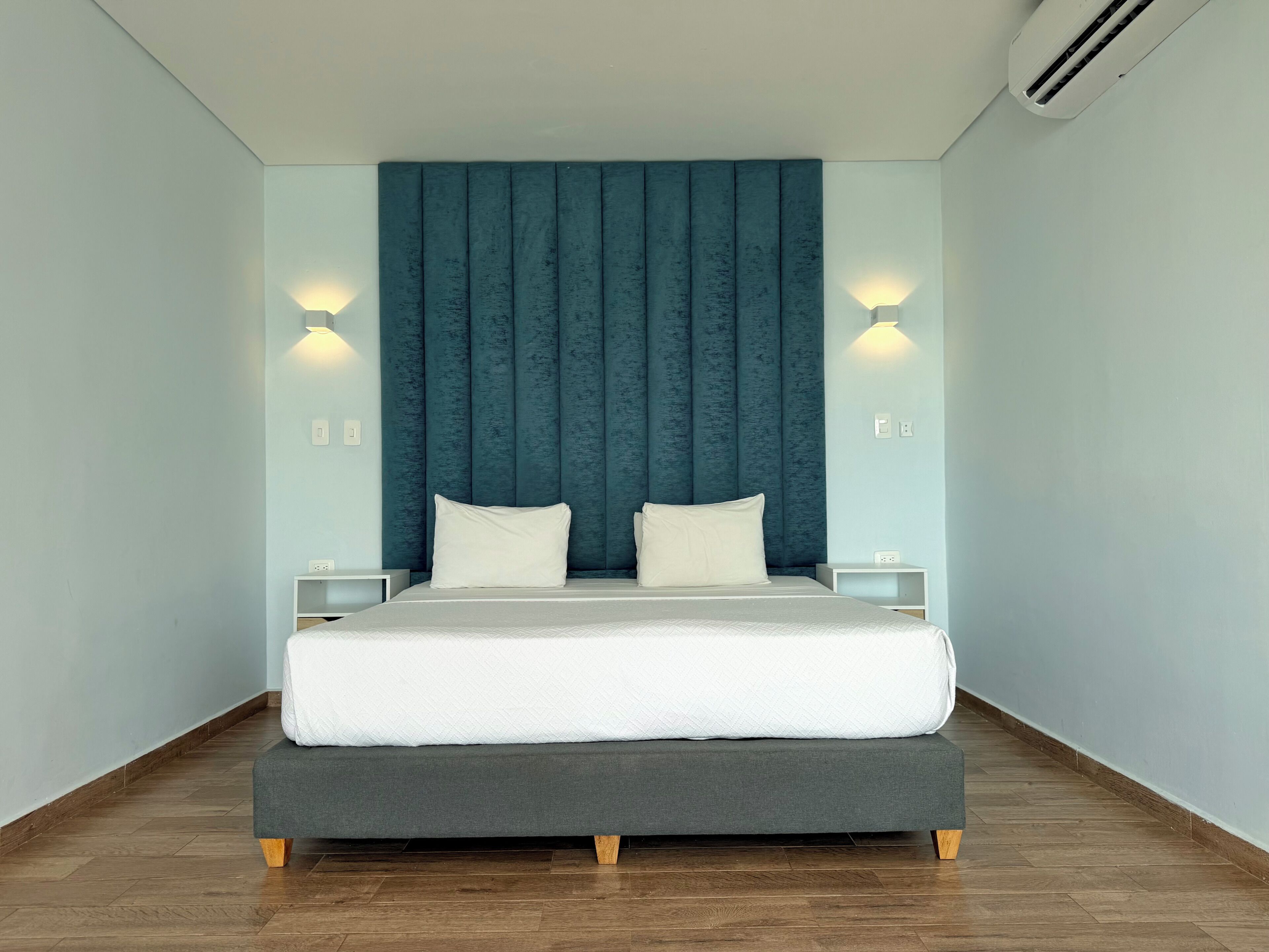 A modern bedroom with a large bed, dark headboard, two bedside tables, and wall-mounted lights.
