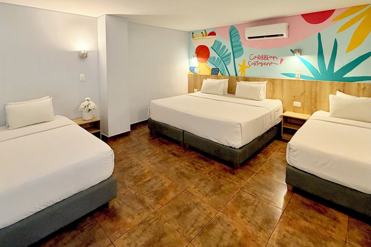 Ein Hotelzimmer mit drei Betten, einem hölzernen Kopfteil, Wandgemälde und einer Decken-Klimaanlage.