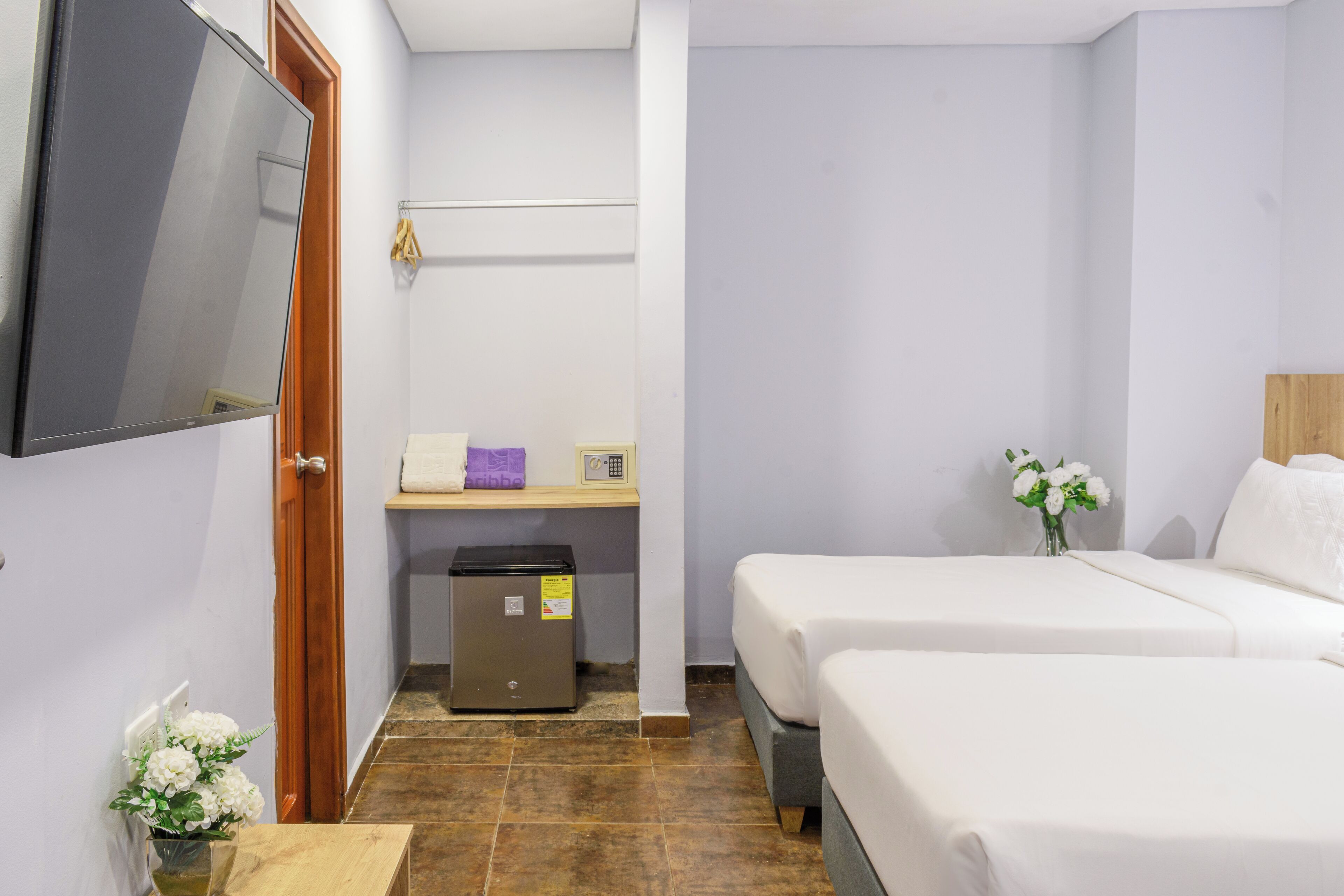 A hotel room with two beds, a small desk with a computer, a TV mounted on the wall, and a trash bin.