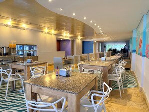 Un hall d’hôtel doté de plusieurs espaces salon, une cuisine à l’arrière-plan et une fresque colorée sur le mur.