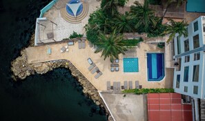 An aerial view of a resort with a pool, lounge chairs, palm trees, and a rocky shoreline. - Hotel Caribbean Cartagena (Cartagena)
