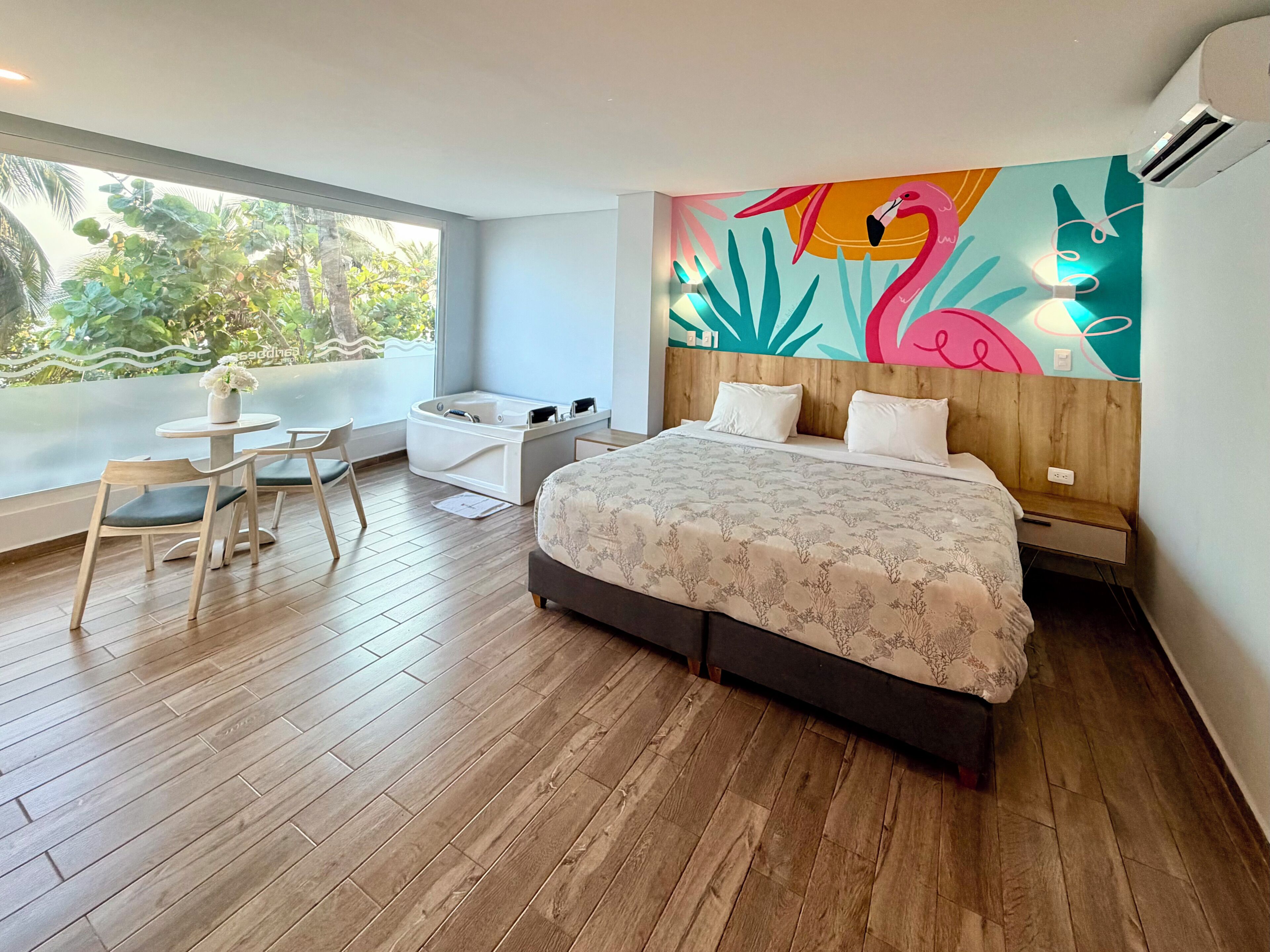 A modern bedroom with a large bed, a small desk with a chair, a jacuzzi tub, and a vibrant wall mural.