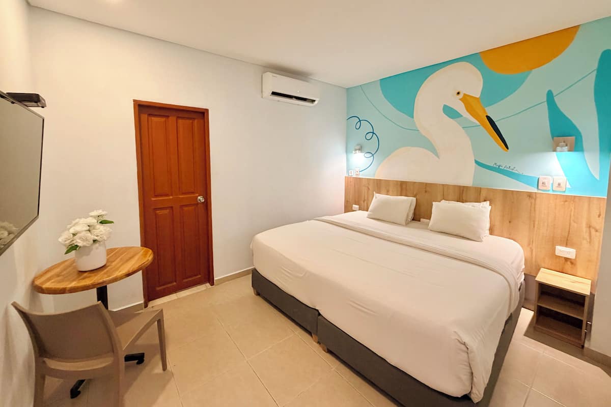 Ein Hotelzimmer mit einem Bett, einer Holztür, einem kleinen Tisch mit einer Vase und einer Wand mit einem Schwan-Fresko.