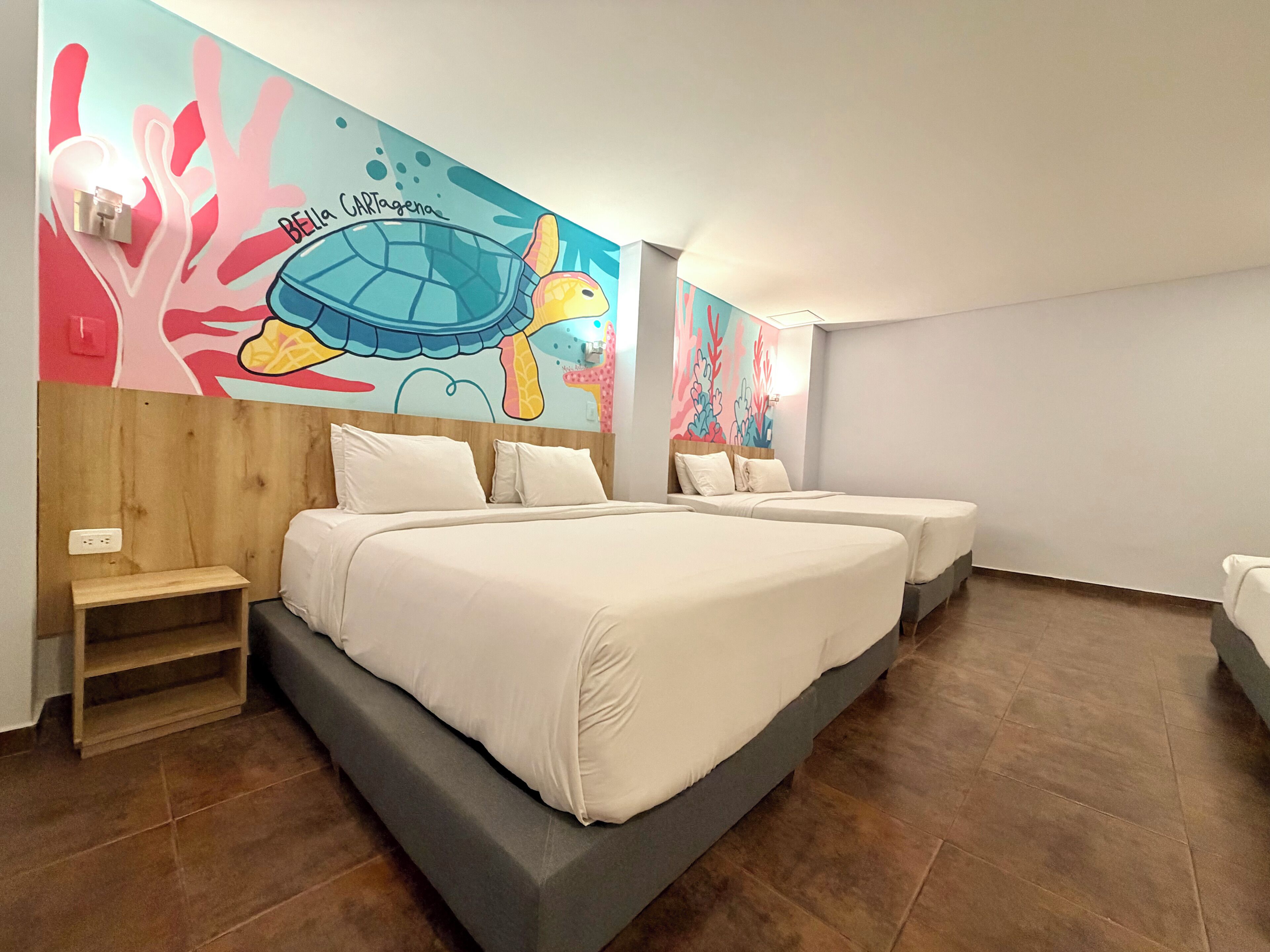 A hotel room with a large bed, two smaller beds, a wooden headboard, a small shelf, and a colorful mural on the wall.