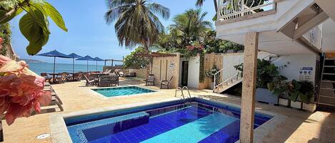A pool area with two pools, lounge chairs, and a view of the sea.