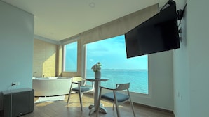 Une chambre moderne dotée d’une grande fenêtre, d’un téléviseur à écran plat, d’une petite table avec des chaises et d’une baignoire.