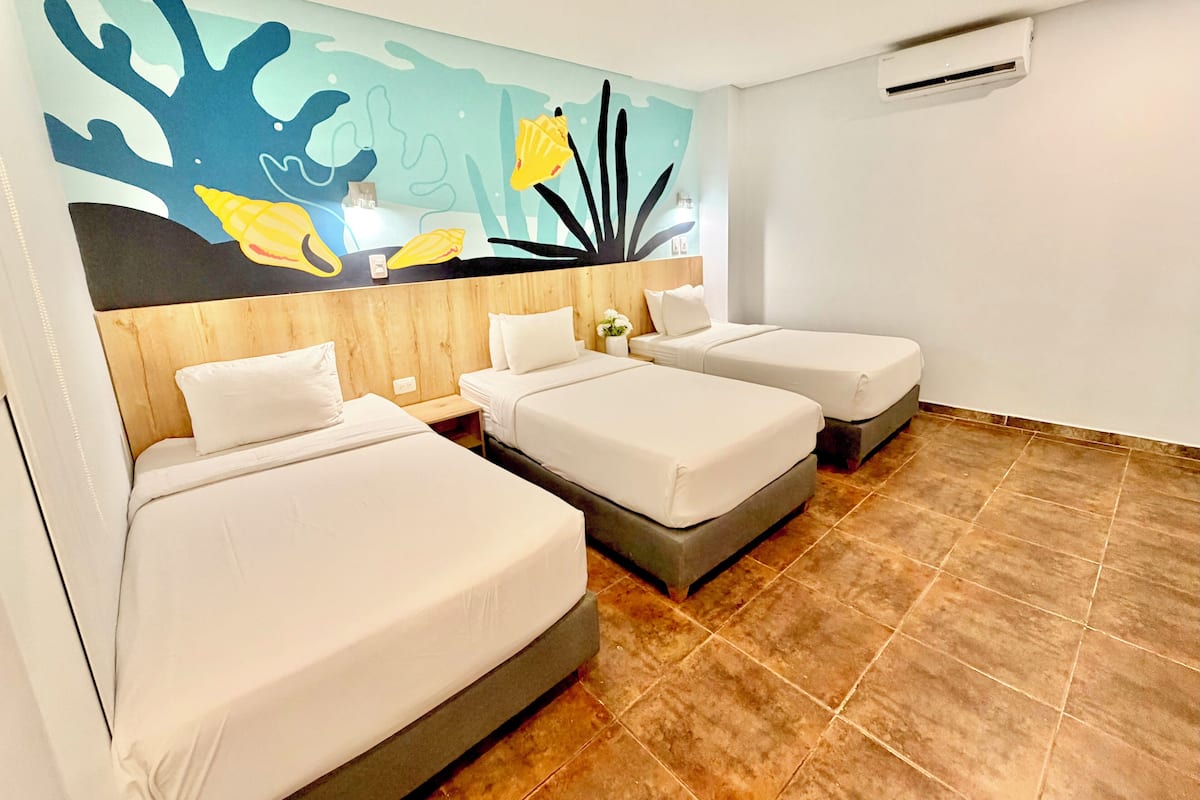 Ein Hotelzimmer mit drei Betten, einer Wandmalerei mit Meereslebewesen, einem Holzkopfende und einem Fliesenboden.