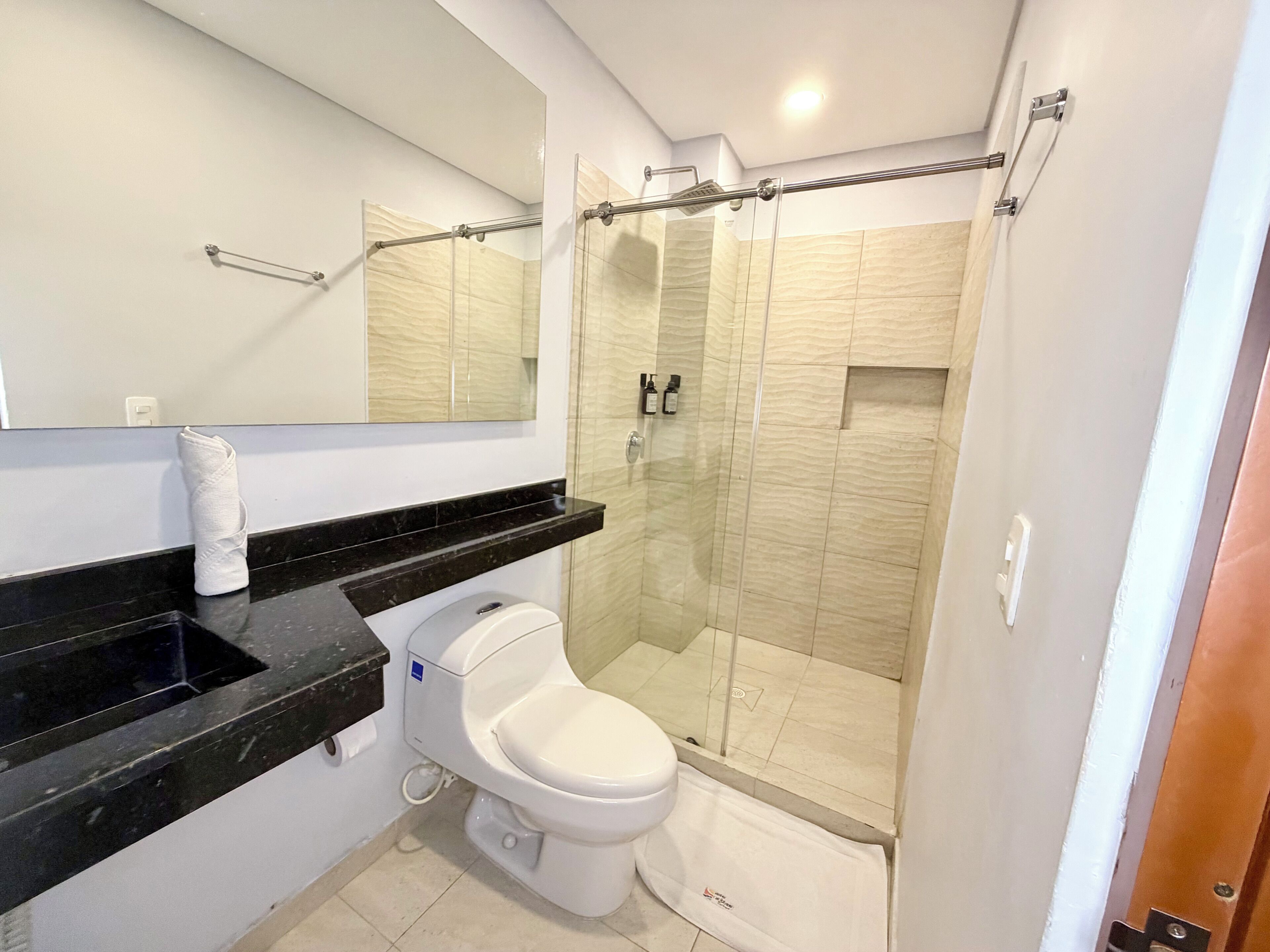 Une salle de bain moderne comprenant des toilettes, un lavabo, une douche en verre et un grand miroir.