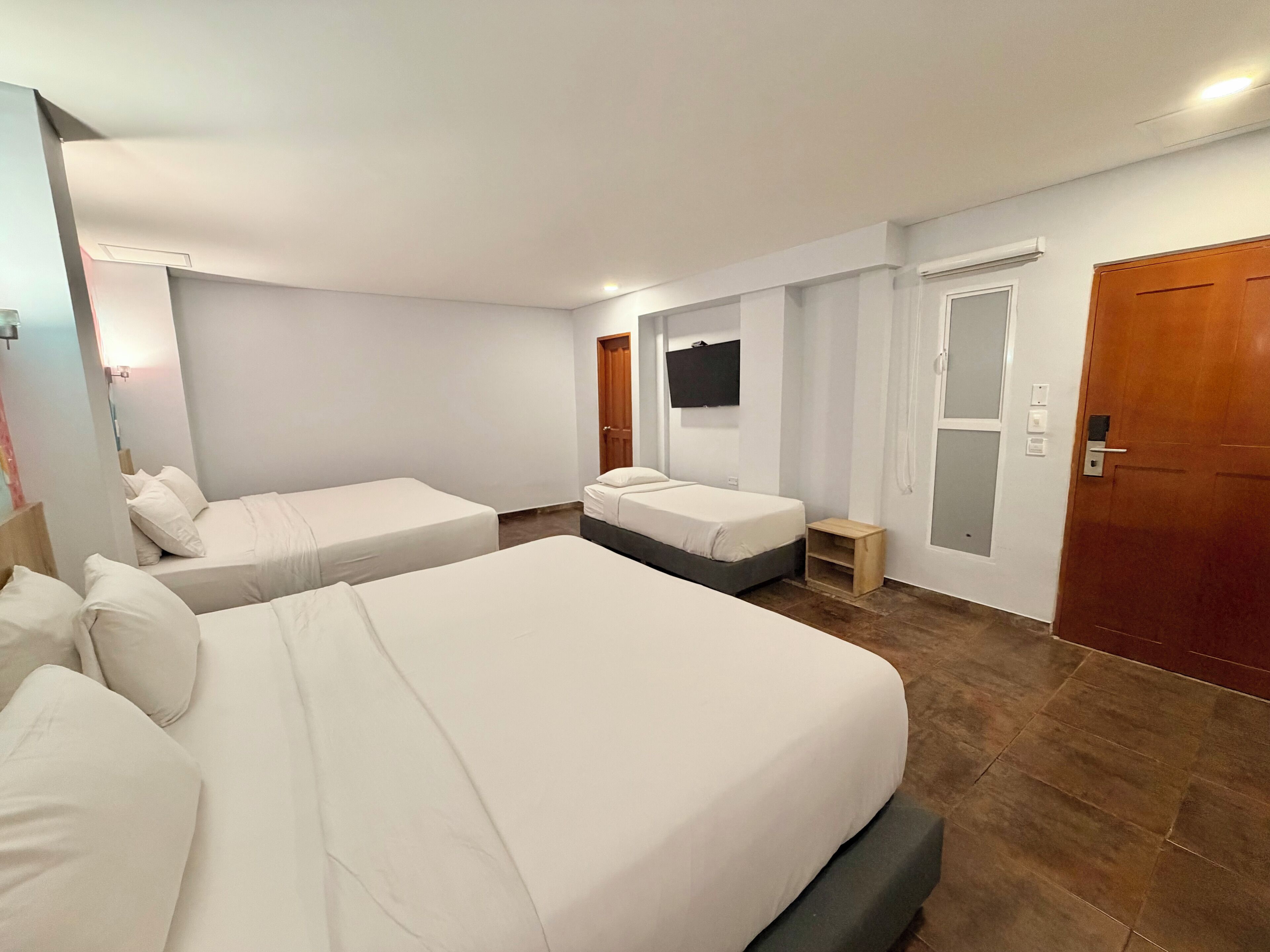 Une chambre d’hôtel avec deux lits, un téléviseur fixé au mur, une porte en bois et une petite table de chevet en bois.
