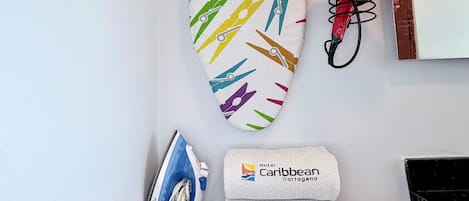A room with a hanging wooden hanger, a red hairdryer, an iron, and two towels with the 'Hotel Caribbean Cartagena' logo.
