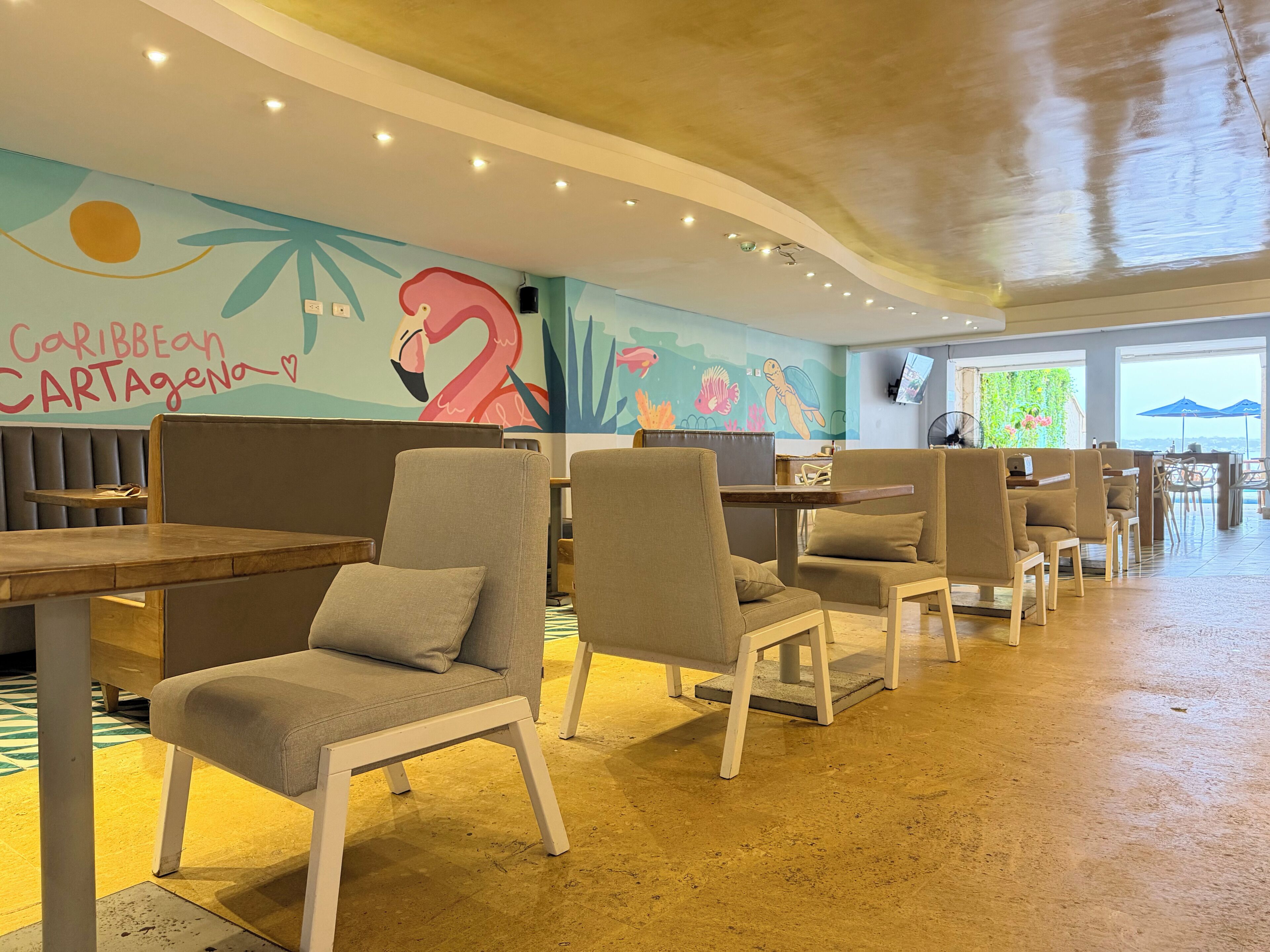 Um restaurante com cabines e mesas, um mural com um flamingo, e vista para o mar.