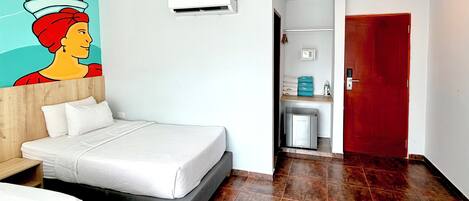 Habitació d'hotel amb llit, aire condicionat fixat a la paret, porta vermella i zona de bany petita.