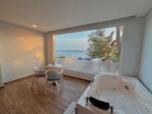 Une pièce dotée d’une grande fenêtre, d’un jacuzzi, d’une petite table avec une chaise et d’une plante.