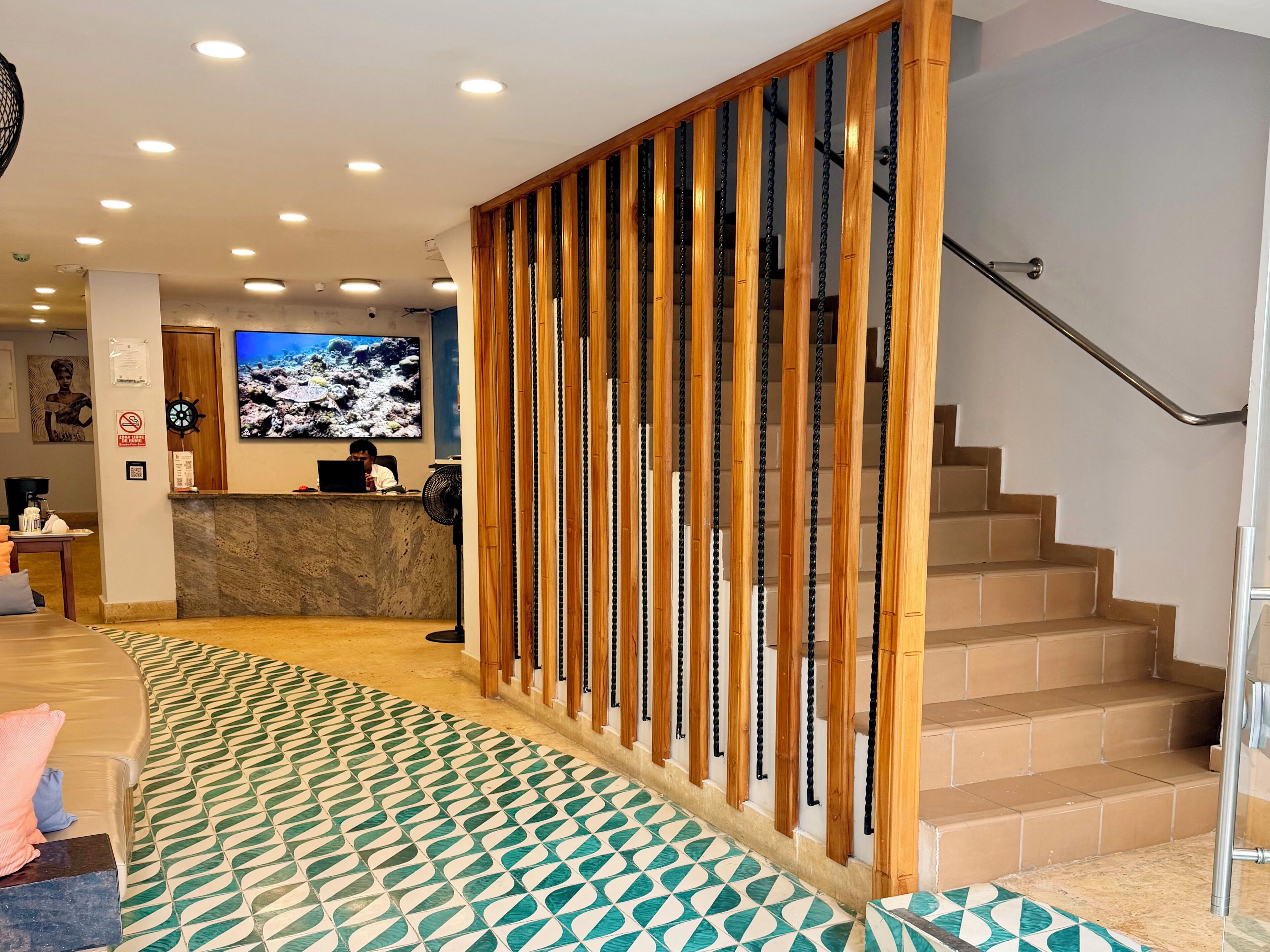 Een hotellobby met een receptiebalie, een televisiescherm, een trap en vloerbekleding met een patroon.