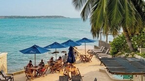 Une terrasse au bord de la plage, dotée de chaises longues et de parasols, avec vue sur la mer.