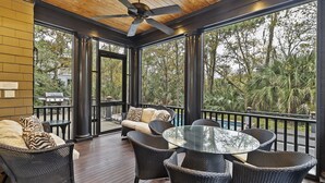 A covered outdoor area with wicker furniture, a glass table, and a ceiling fan.