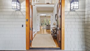 A hallway with white brick walls, wooden doors, and a rug leading to a seating area.
