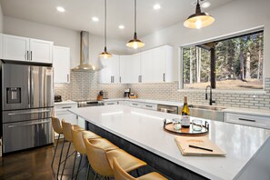 A modern kitchen with stainless steel appliances, white cabinetry, and a large island with bar stools. - Forested Oasis for the Whole Family- Pet Friendly! Game Room, Hot tub and more!  (Ronald)
