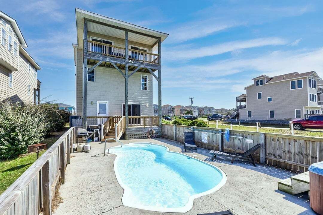 Een woongebied met een zwembad, een houten terras en een twee verdiepingen tellend gebouw met balkon.