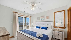 Una camera da letto con un letto grande, una ventola a soffitto, un comodino, una finestra con tende e opere d'arte appese al muro.