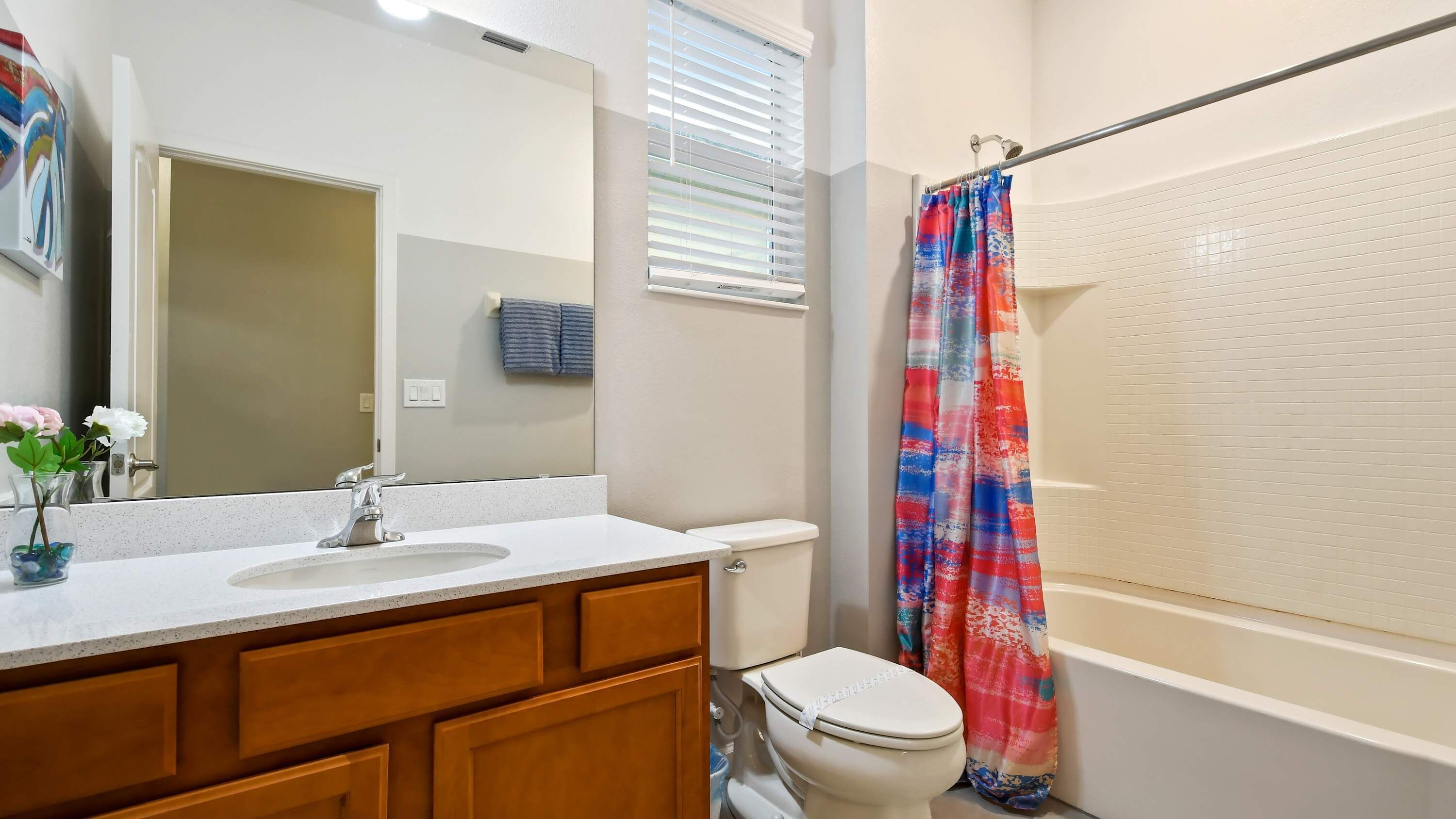 Un baño con lavamanos blanco, tocador de madera, inodoro y cortina de ducha.