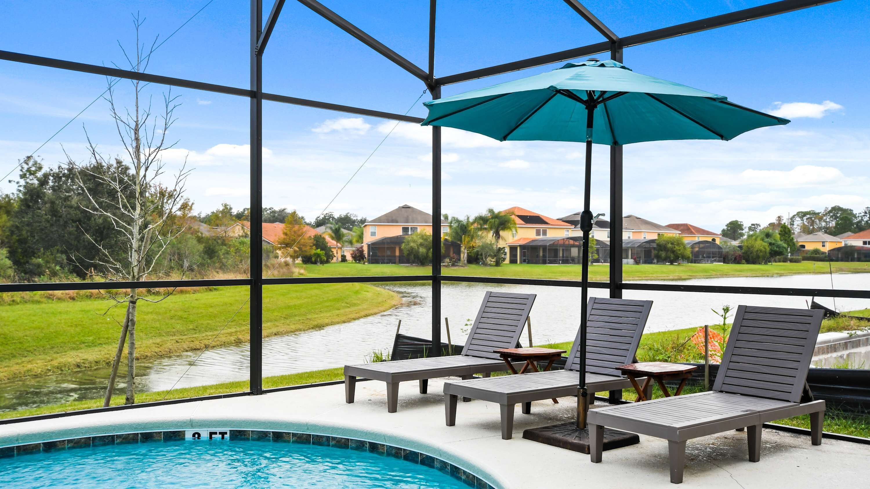 A poolside area with lounge chairs and an umbrella, overlooking a residential neighborhood.