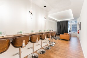 A modern dining area with a long wooden table, bar stools, and a sofa.