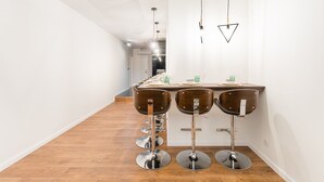 Une cuisine moderne dotée d’un long comptoir, de quatre tabourets de bar et de luminaires suspendus.