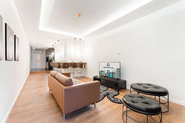 A modern living room with a sofa, two black bar stools, a TV, and a dining area with chairs and a table.